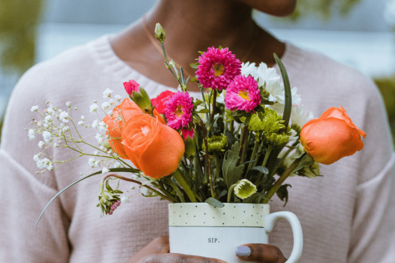 A woman holding a cup filled with colorful flowers
