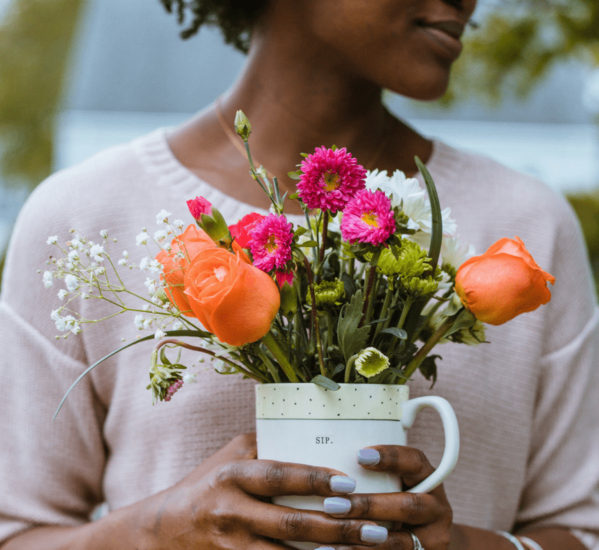 A woman holding a cup filled with colorful flowers